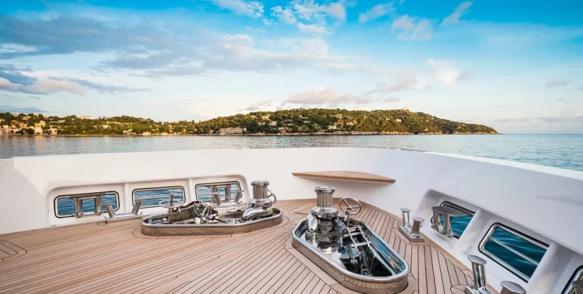 Teak yacht deck on the bow of a superyacht looking out on an island and blue seas.