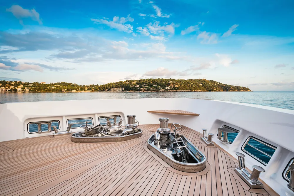 Teak yacht deck on the bow of a superyacht looking out on an island and blue seas.