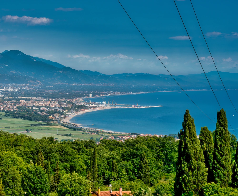 Beautiful view of the marina de Carrara. It is a clear blue sky and bright blue waters with greenery leading towards the marina.